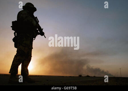 Un soldat britannique de l'Artillerie royale du 29 Commando Regiment est en service de garde, alors qu'un feu de pétrole brûle à l'horizon dans le sud de l'Irak. Alors que le conflit irakien entre dans sa deuxième semaine. Banque D'Images