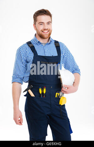 Cheerful handsome young builder dans debout et tenant ensemble casque Banque D'Images