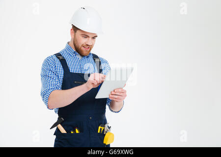 Heureux jeune barbu builder en casque et dans l'ensemble à l'aide de tablet Banque D'Images