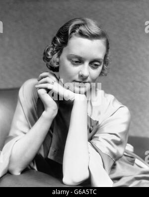 1930 PORTRAIT PENSIVE WOMAN SITTING IN CHAIR LEANING CHIN SUR PENSÉE MAIN Banque D'Images