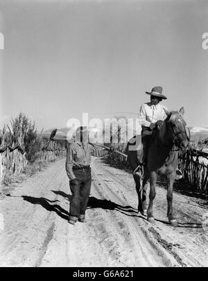 Années 30, deux hommes vivent DES INDIENS SUR LA ROUTE DU DÉSERT À CHEVAL D'AUTRES MARCHER PARLER SAN ILDEFONSO PUEBLO NOUVEAU MEXIQUE USA Banque D'Images