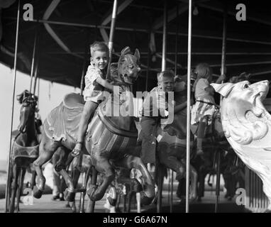 1950 ENFANTS SUR CAROUSEL 2 SMILING BOYS LEANING À CÔTÉ DE CHEVAUX DE TOURNER Banque D'Images