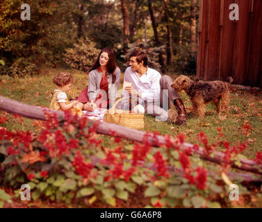 1970 FAMILLE MAMAN PAPA GIRL PET DOG HAVING PICNIC IN BACKYARD Banque D'Images