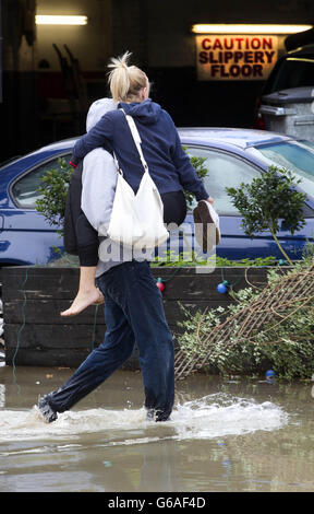 Un homme aide une dame à travers l'eau sur Half Moon Lane à Herne Hill, Londres comme un plan d'eau en rafale a entraîné de graves inondations avec de l'eau jusqu'à un mètre de profondeur dans certains endroits Banque D'Images