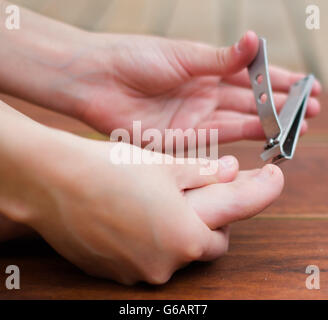 Couper les ongles de pieds en métal clipper, mains aidant dans un fond de bois Banque D'Images