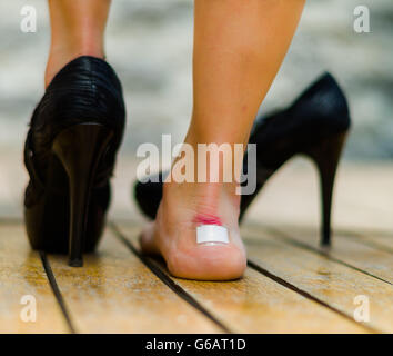 High heels fait mal très souvent, les pieds avec peu de blanc patch sur la cheville, un pieds sur le plancher et d'autres avec des chaussures noires Banque D'Images