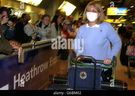 Sandra Perry, de Sutton, Surrey, porte un masque facial lorsqu'elle revient à l'aéroport d'Heathrow, sur un vol en provenance de Beijing, Chine. *..le gouvernement a été exhorté à classer le SRAS en regard du choléra et de la variole afin que les personnes arrivant au Royaume-Uni avec des symptômes puissent être détenues pour traitement comme le secrétaire de la Santé de l'ombre le Dr Liam Fox a déclaré que la réponse de la Grande-Bretagne jusqu'à présent à l'épidémie avait été « faible, complaisante et irresponsable ». Mais le médecin-chef Sir Liam Donaldson a déclaré que les six affaires en Grande-Bretagne jusqu'à présent avaient été détectées rapidement et maîtrées. Banque D'Images