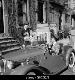 Années 1950 Années 1960 DEUX BUSINESSMEN TALKING SUR STREET one sitting in convertible deux places de voiture de sport anglais Banque D'Images