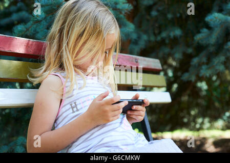 Belle fille blonde Woman sitting on ancien banc de parc jouant sur smart phone Banque D'Images