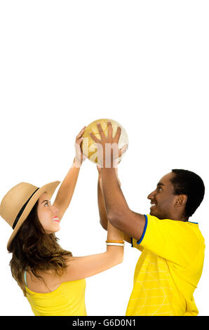 Charmant couple interracial portant des maillots de football jaune holding ball dans l'air entre eux, angle fond studio blanc profil Banque D'Images