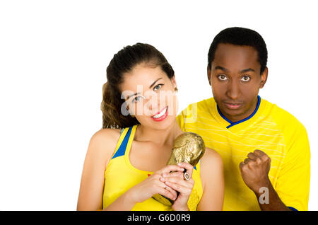 Charmant couple interracial portant des maillots de football jaune petit HOLDING TROPHY qui pose pour appareil photo, fond studio blanc Banque D'Images