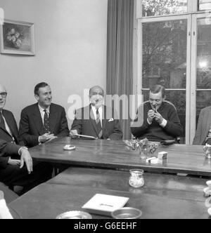 Vêtu de façon informelle d'un chandail bleu, M. ANTHONY WEDGWOOD BENN, le ministre des postes, allume son tuyau au début souriant des discussions dans le salon de sa maison de Londres à Holland Park Avenue, à Notinghill, À la télévision, des arrangements ont été pris pour le championnat du monde de lutte entre Cassius Clay et Henry Cooper à Londres le 21 mai. Sur la photo se trouvent l'ancien capitaine de cricket de l'Angleterre, M. TED DEXTER, directeur exécutif de Viewsport Ltd., et M. HARRY LEVENE, le promoteur du combat. Des représentants de la BBC, de l'ITV et de la télévision payante ont également participé aux entretiens. Banque D'Images