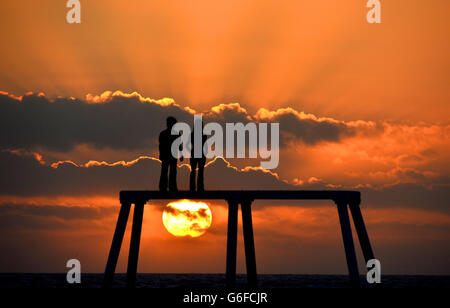 Le soleil se lève sur la sculpture géante d'un homme et d'une femme situé à 300 mètres de la mer au large de la côte de Northumberland à Newbiggin-by-the-Sea. Composée de deux figures de bronze de 5 mètres de haut d'un homme et d'une femme, la sculpture est appelée « le couple » et est réalisée par l'artiste Sean Henry. Banque D'Images
