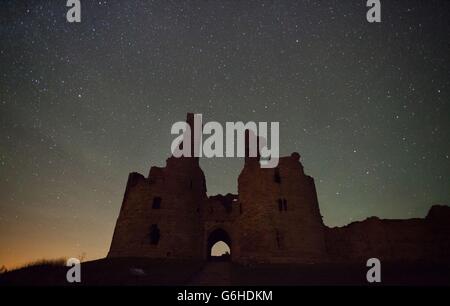 Une nuit claire montrant un ciel étoilé au-dessus du château de Dunstanburgh dans le Northumberland. Banque D'Images