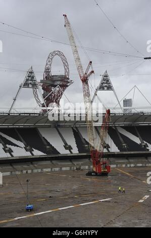 Deux ouvriers de la construction traversent l'ancien terrain d'athlétisme au stade Queen Elizabeth Olympic Park, à Stratford est de Londres, tandis qu'une grue de levage lourde est inactive après que les conditions météorologiques aient retardé le retrait des premiers panneaux de projecteurs,Alors que le travail commence au transformer en un lieu polyvalent tout au long de l'année et la résidence permanente du West Ham United football Club et du nouveau stade de compétition national pour UK Athletics. Banque D'Images