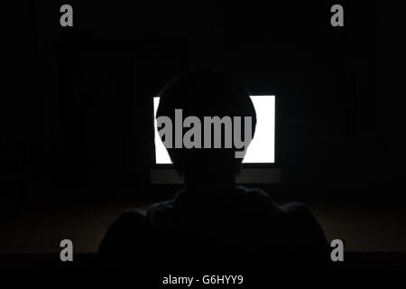 Silhouette de jeune homme assis à la table et à l'aide d'écran vide coffre dans la pièce sombre Banque D'Images
