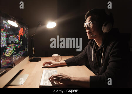 Heureux bel asiatique homme gamer jouant à la table de jeu d'ordinateur dans une pièce sombre Banque D'Images