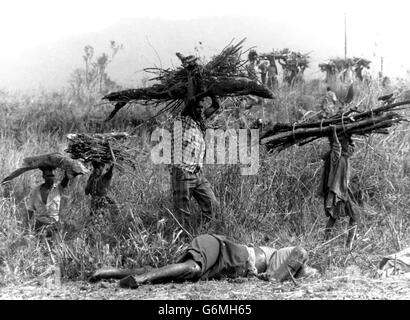 CONTENU GRAPHIQUE : les réfugiés rwandais, transportant du bois, passent par un corps (premier plan) lorsqu'ils retournent au camp de réfugiés de Kikumba, à 30 km au nord de Goma, Zaïre. Banque D'Images