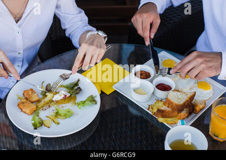 Les gens d'affaires libre de mains, hommes et femmes ayant le petit déjeuner au café en plein air. Repas avec salade, omelette, bacon. Banque D'Images