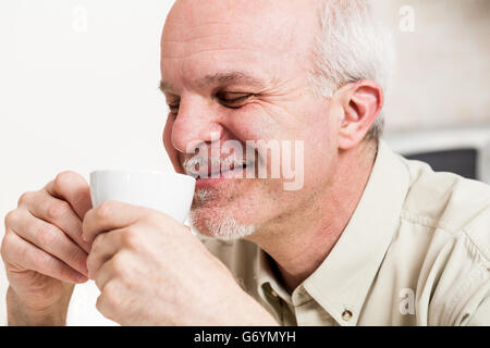 Close up sur seul beau bearded man avec les yeux fermés et sourire satisfait en sirotant du café d'une petite tasse de thé blanc Banque D'Images