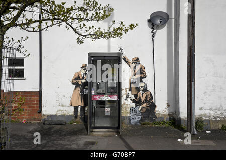 Le nouveau graffiti Street art pièce, suspecté d'être un Banksy, qui est apparu sur le côté d'une maison sur Fairview Road à côté de St. Anne's Terrace, Cheltenham.L'œuvre, qui montre trois personnages à l'écoute d'une conversation dans une boîte téléphonique, se trouve à quelques kilomètres seulement des responsables des communications gouvernementales (GCHQ), qui est responsable de fournir des renseignements sur les signaux et de l'assurance de l'information au gouvernement britannique et aux forces armées. Banque D'Images