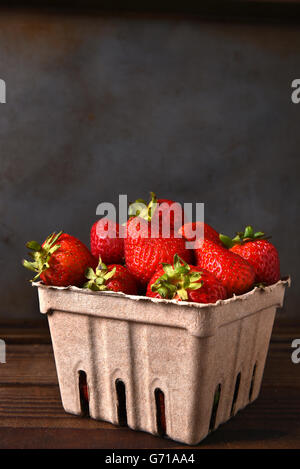 La vie encore d'une production de carton récipient plein de fraises fraîches cueillies sur une table en bois. Format vertical avec copie espace. Banque D'Images
