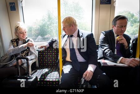 Le maire de Londres Boris Johnson offre à un passager quelques bleuets alors qu'il est assis à côté du Premier ministre David Cameron sur un train souterrain, alors qu'il se rend à Westminster après avoir visité le Harrow Skills Center et rencontré des acheteurs locaux dans le centre-ville de Harrow lorsqu'ils ont pris le sentier de campagne ensemble. Banque D'Images