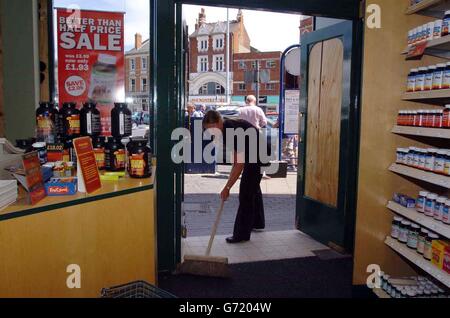 Caroline Spencer, responsable du magasin d'alimentation de la région Holland & Barrett à Boston, Lincs, balaie le verre brisé, après que les fans de football furieux de la défaite spectaculaire de l'Euro 2004 par la France ont pris le dessus dans la ville. Deux voitures de police ont été renversée et incendiées après que les problèmes se sont aggravés à l'extérieur du pub STILL, et un groupe de 70 personnes, ainsi que des groupes plus petits répartis dans la ville, ont lancé des briques et des bouteilles aux policiers. A côté de Holland & Barrett, le Thresher Wine Shop était allumé et raillé. La police de la ville a procédé à 11 arrestations, dont six pour troubles violents, deux pour vol, deux Banque D'Images