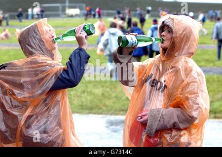 (G-D) Joanna Kenna, 22 ans, de Bray, Co Wicklow, et Gillian Allsop, de Shankill, Co Dublin, prennent un verre d'eau sous une douche de pluie, avant d'entrer dans le festival Oxegen, à l'hippodrome de Punchestown, Co Kildare, Irlande. On estime à 60,000 le nombre de personnes à venir pour le plus grand festival de musique annuel d'Irlande, avec près de 48,000 de ces campeurs. Environ 100 groupes se produisent au cours de l'événement de deux jours, y compris le groupe New Yortk, le groupe Strokes et le groupe English, The Darkness. Banque D'Images