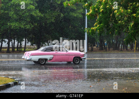 Pink vintage American Classic car la conduite sur route mouillée dans une pluie d'été à La Havane, Cuba Banque D'Images