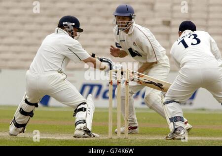 Ian Bell, batteur du Warwickshire, coupe la balle entre Iain Sutcliffe du Lancashire et Jamie Haynes, gardien de cricket, lors du match de la Frizzell County Championship Division One à Old Trafford. Banque D'Images