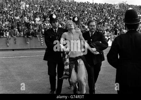 Porté à la taille, un homme est conduit par la police au sol de Brisbane Road avant le match de la Ligue Division 2 entre Orient et Manchester United le jour de l'ouverture de la saison 1974/75. Banque D'Images