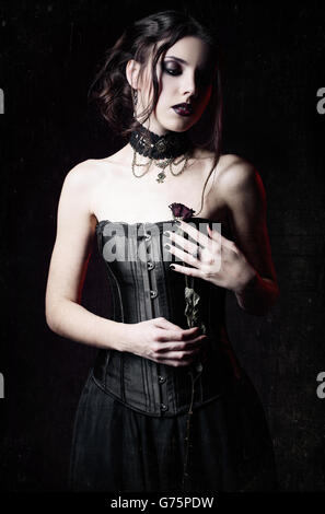 Portrait dramatique de la belle triste goth girl holding a withered rose dans les mains. Effet texture Grunge Banque D'Images