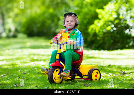 Cute boy wearing safety helmet équitation son tricycle en parc d'été ensoleillé. Les enfants circuler à bicyclette. Premier vélo pour petit enfant. Banque D'Images