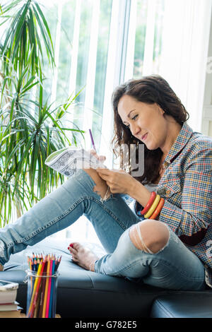 Jeune fille à se libérer du stress avec passe-temps créatif, Coloring Book Inn salle de séjour Banque D'Images