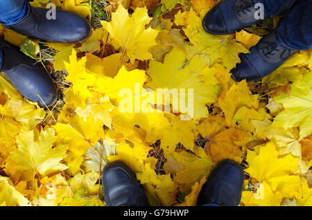 Vue de dessus d'un pied dans l'automne de la famille des bottes de trois personnes, qui se tiennent sur la pelouse recouverte de feuilles d'érable tombé jaune Banque D'Images