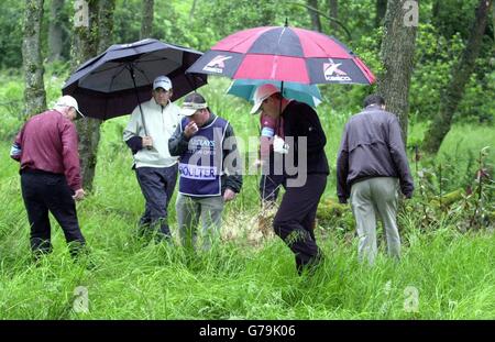 Gary Orr (parapluie rouge et noir), en Écosse, cherche sa balle de golf perdue et est aidé dans sa recherche par Ian Poulter (blouson blanc), en Angleterre, sur le premier trou lors de la première partie de l'Open écossais de Barclays au club de golf Loch Lomond près de Balloch.La lecture a été suspendue plus tard en raison de la météo. Banque D'Images