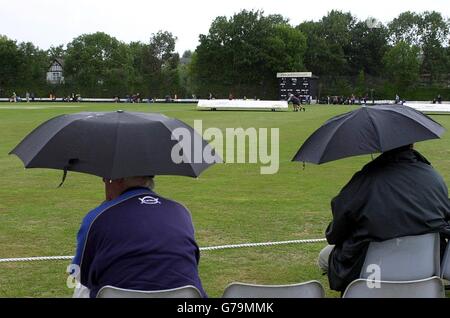 Les spectateurs ont mis leurs parapluies pendant que la pluie s'arrête, pendant le match de championnat du comté de Frizzell entre Surrey et Middlesex à Guildford. Banque D'Images