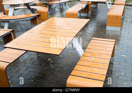 Focus sélectif des tables de café en plein air humide dans la rue après une chute de pluie sur la chaussée mouillée avec un peu de jaune les feuilles tombées. Banque D'Images