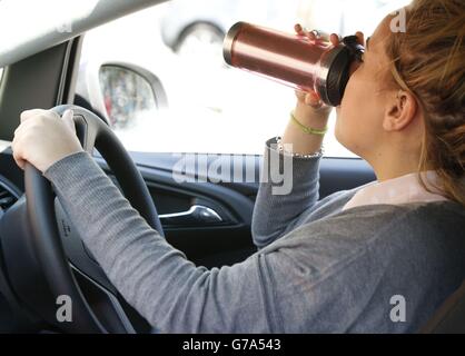 IMAGE POSÉE PAR LE MODÈLE UNE femme boit du café en conduisant. Banque D'Images