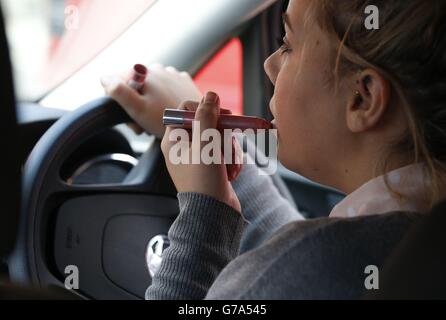 IMAGE POSÉE PAR LE MODÈLE UNE femme applique un rouge à lèvres pendant la conduite. Banque D'Images