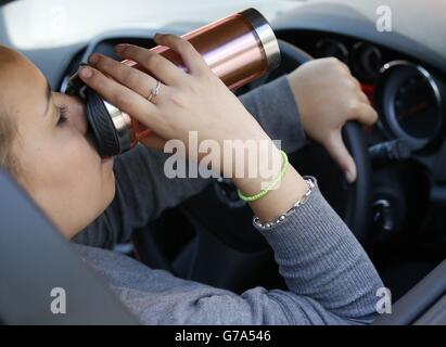 Stock moteur.IMAGE POSÉE PAR LE MODÈLE Une femme boit du café en conduisant. Banque D'Images