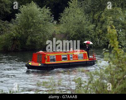 Un bateau étroit se déplace le long de la Tamise près de Staines-upon-Thames à Surrey sous une forte pluie. Banque D'Images