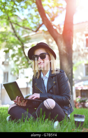 Hipster girl sitting on grass with laptop Banque D'Images