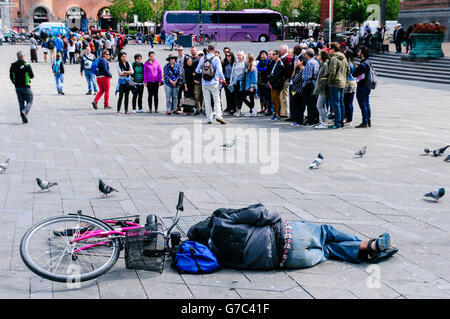 Un homme ivre dort sur une place publique à côté de son vélo, comme un groupe de touristes regardent à Copenhague, au Danemark Banque D'Images