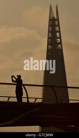 Un homme prend une photo sur le Millennium Bridge avec le bâtiment Shard en arrière-plan au lever du soleil à Londres. Banque D'Images