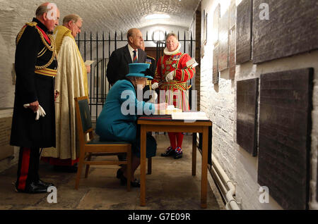 La reine Elizabeth II signe le livre des visiteurs à la chapelle royale de Saint-Pierre ad Vincula comme duc d'Édimbourg (au centre), gendarme de la Tour, général le Seigneur Dannatt (à gauche) et le révérend Canon Roger Hall (à gauche) Regardez pendant une visite de la Tour de Londres pour voir l'installation de Blood balayées terres et les mers de Rouge, qui marque le centenaire de l'éclatement de la première Guerre mondiale. Banque D'Images