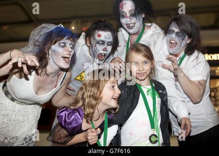 Kayla Harrison (à gauche) et Molly Tracey d'Ealing rencontrent des gens habillés comme des zombies après avoir participé à une course de zombies au centre commercial Ealing Broadway dans l'ouest de Londres, pour recueillir de l'argent pour la charité locale - la cabane en rondins. Banque D'Images