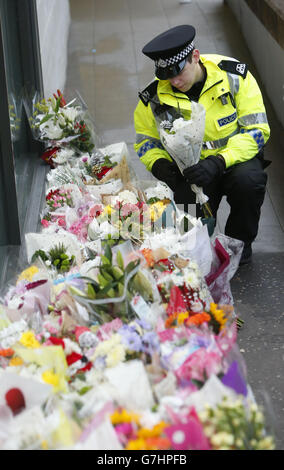 Un policier regarde des fleurs près de la scène à George Square, à Glasgow, où un camion-benne s'est écrasé sur un groupe de piétons qui a fait six morts. Banque D'Images