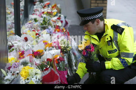 Un policier regarde des fleurs près de la scène à George Square, à Glasgow, où un camion-benne s'est écrasé sur un groupe de piétons qui a fait six morts. Banque D'Images